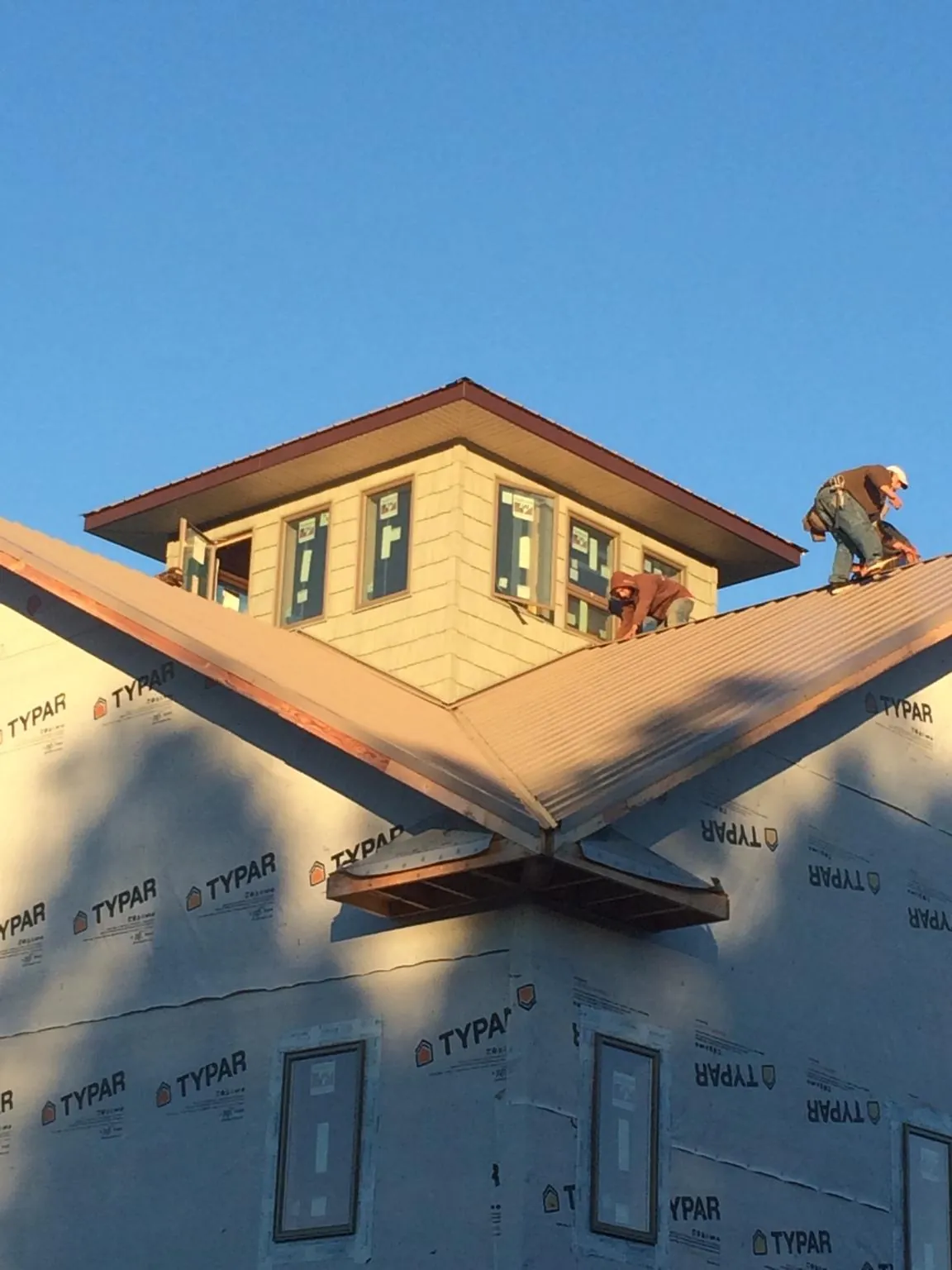Roofers working around a rooftop cupola on a new metal roof at sunset — Roof Waterproofing in Stanley by Roofing Brothers